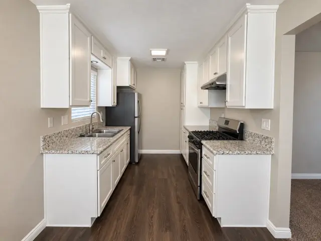 Galley kitchen with white cabinets, a gas range and a stainless steel refrigerator